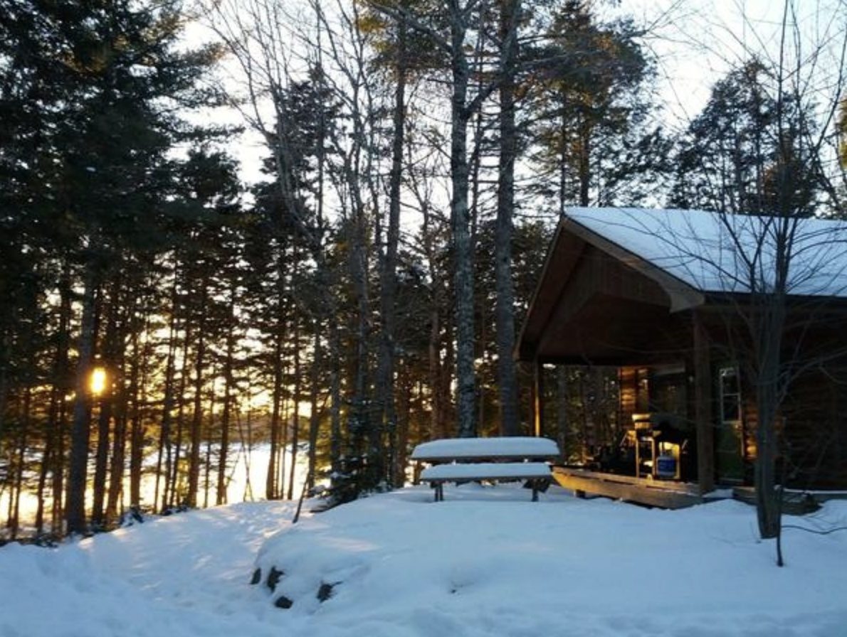 A snow-covered cabin and picnic table in the woods