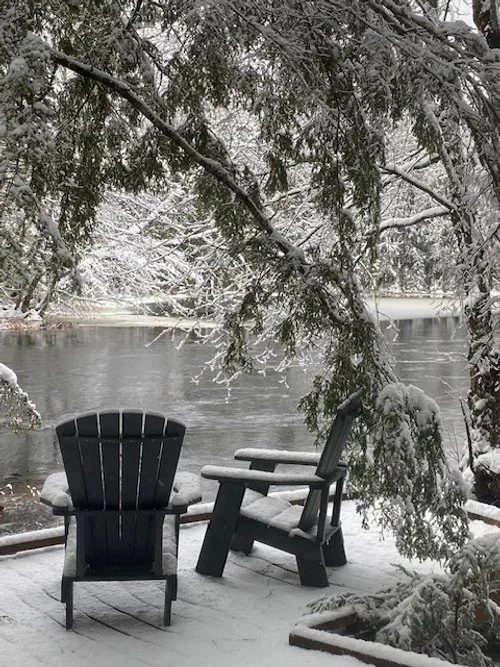 Two Adirondack chairs beside a snowy river